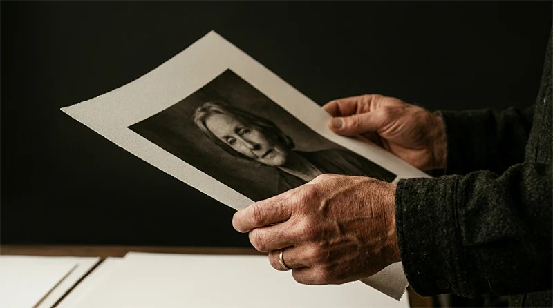 Mains d'un photographe professionnel tenant avec soin un tirage d'art mat d'un portrait noir et blanc en studio.